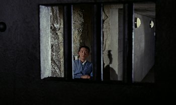 Movie still from “Goldfinger” (1964), directed by Guy Hamilton – A man in a suit sitting in a jail cell; Wide shot, High angle