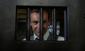 Movie still from “Goldfinger” (1964), directed by Guy Hamilton – A person behind bars in a jail cell; Close Up shot, Low angle
