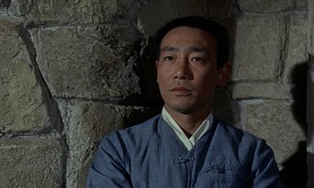 Movie still from “Goldfinger” (1964), directed by Guy Hamilton – A man in a blue shirt is standing in front of a stone wall; Close Up shot, High angle