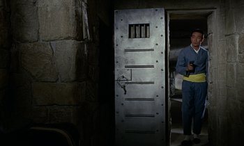Movie still from “Goldfinger” (1964), directed by Guy Hamilton – A man standing in front of a metal door in a room; Wide shot, High angle