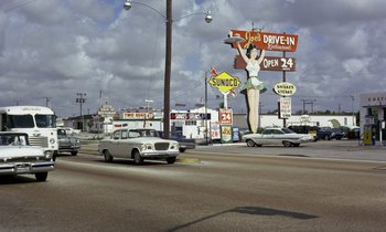 Movie still from “Goldfinger” (1964), directed by Guy Hamilton – Cars driving down a street with a lot of signs on the side of the road; Extreme Wide shot, High angle