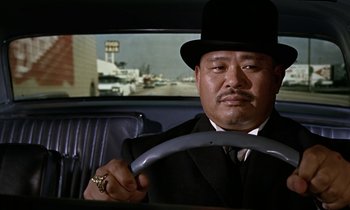 Movie still from “Goldfinger” (1964), directed by Guy Hamilton – A man in a suit and a hat driving a car; Close Up shot, Over the shoulder angle