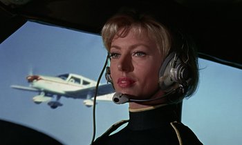 Movie still from “Goldfinger” (1964), directed by Guy Hamilton – A woman in a helicopter with a plane in the background; Close Up shot, Low angle