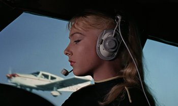 Movie still from “Goldfinger” (1964), directed by Guy Hamilton – A young girl wearing headphones and a headset in an airplane cockpit; Close Up shot, Low angle