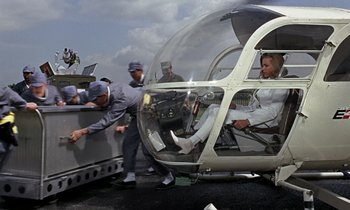 Movie still from “Goldfinger” (1964), directed by Guy Hamilton – A man and a woman in a helicopter on the ground; Wide shot, High angle