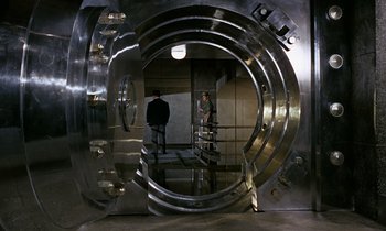 Movie still from “Goldfinger” (1964), directed by Guy Hamilton – Two men standing inside a large metal door; Wide shot, High angle
