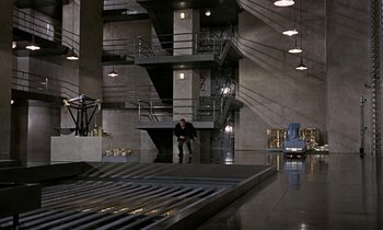 Movie still from “Goldfinger” (1964), directed by Guy Hamilton – A man standing on a platform in front of a building; Extreme Wide shot, High angle