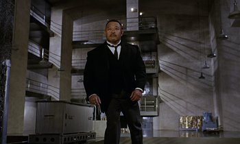 Movie still from “Goldfinger” (1964), directed by Guy Hamilton – A man in a suit and tie standing in a room; Wide shot, Low angle