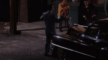Movie still from “Goodfellas” (1990), directed by Martin Scorsese – A man in a gray suit standing in front of a car; Wide shot, High angle