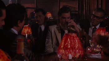 Movie still from “Goodfellas” (1990), directed by Martin Scorsese – A man drinking a glass of wine at a party; Medium shot, Over the shoulder angle