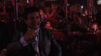 Movie still from “Goodfellas” (1990), directed by Martin Scorsese – A man in a suit and tie holding a glass of wine; Medium shot, Over the shoulder angle