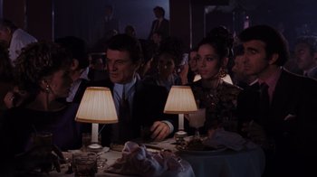 Movie still from “Goodfellas” (1990), directed by Martin Scorsese – A group of people sitting at a table with lamps; Medium shot, Over the shoulder angle
