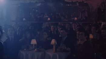 Movie still from “Goodfellas” (1990), directed by Martin Scorsese – A group of people sitting at tables in front of a projector screen; Wide shot, High angle