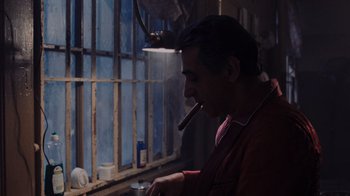 Movie still from “Goodfellas” (1990), directed by Martin Scorsese – A man smoking a cigar in front of a window; Medium shot, Over the shoulder angle