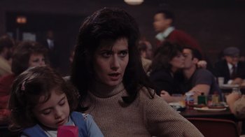 Movie still from “Goodfellas” (1990), directed by Martin Scorsese – A woman with long hair is sitting at a table with a little girl; Close Up shot, Over the shoulder angle