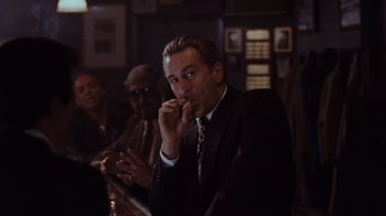 Movie still from “Goodfellas” (1990), directed by Martin Scorsese – A man in a suit is smoking a cigarette; Medium shot, Over the shoulder angle