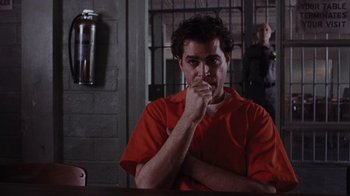 Movie still from “Goodfellas” (1990), directed by Martin Scorsese – A man in an orange shirt sitting at a table in a jail cell; Medium shot, Low angle
