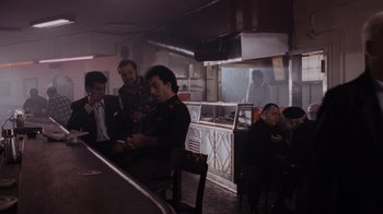 Movie still from “Goodfellas” (1990), directed by Martin Scorsese – A group of men sitting at a table in front of a counter; Wide shot, High angle