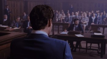 Movie still from “Goodfellas” (1990), directed by Martin Scorsese – A man in a suit is sitting in front of a group of people; Medium shot, Over the shoulder angle