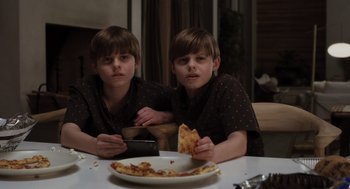 Movie still from “Goodnight Mommy” (2022), directed by Matt Sobel – Two young boys sitting in front of a plate of pizza; Medium shot, High angle