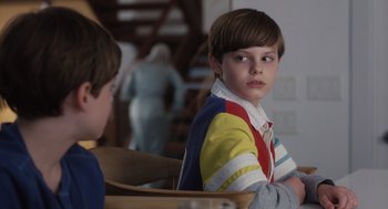 Movie still from “Goodnight Mommy” (2022), directed by Matt Sobel – A young boy sitting at a table with another young boy; Close Up shot, Over the shoulder angle