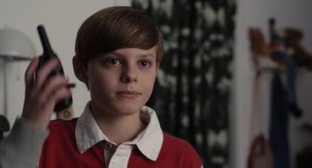 Movie still from “Goodnight Mommy” (2022), directed by Matt Sobel – A young boy in a red shirt is looking at the camera; Close Up shot, Over the shoulder angle