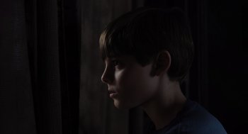 Movie still from “Goodnight Mommy” (2022), directed by Matt Sobel – A young boy looking into the distance in the dark; Close Up shot, Low angle