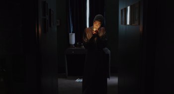 Movie still from “Goodnight Mommy” (2022), directed by Matt Sobel – A person standing in a room lit up by a candle; Medium shot, Low angle