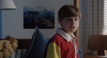 Movie still from “Goodnight Mommy” (2022), directed by Matt Sobel – A boy in a red and yellow shirt is posing for a picture; Close Up shot, Over the shoulder angle