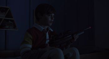 Movie still from “Goodnight Mommy” (2022), directed by Matt Sobel – A young boy holding a gun while sitting in a chair; Medium shot, High angle