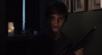 Movie still from “Goodnight Mommy” (2022), directed by Matt Sobel – A young boy holding a gun in a dark room; Close Up shot, High angle