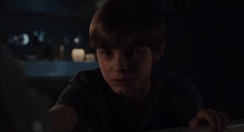 Movie still from “Goodnight Mommy” (2022), directed by Matt Sobel – A young boy is sitting in a dark room; Close Up shot, High angle