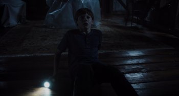 Movie still from “Goodnight Mommy” (2022), directed by Matt Sobel – A boy sitting on the ground in a dark room; Wide shot, High angle