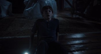 Movie still from “Goodnight Mommy” (2022), directed by Matt Sobel – A boy sitting on the ground in a dark room; Medium shot, High angle