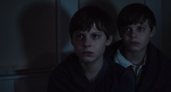 Movie still from “Goodnight Mommy” (2022), directed by Matt Sobel – Two young boys sitting next to each other in a dark room; Close Up shot, Low angle