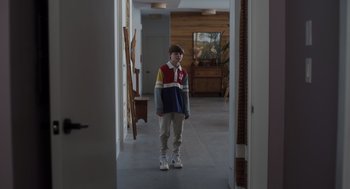 Movie still from “Goodnight Mommy” (2022), directed by Matt Sobel – A person standing in a room with a painting on the wall behind them; Wide shot, Over the shoulder angle