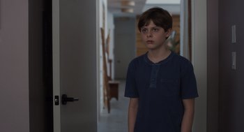 Movie still from “Goodnight Mommy” (2022), directed by Matt Sobel – A young boy standing in front of an open door; Medium shot, Over the shoulder angle