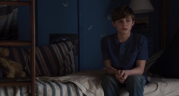 Movie still from “Goodnight Mommy” (2022), directed by Matt Sobel – A young boy sitting on a bed in a bedroom; Medium shot, High angle