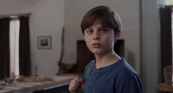 Movie still from “Goodnight Mommy” (2022), directed by Matt Sobel – A young boy holding a green object in his hand; Close Up shot, Low angle