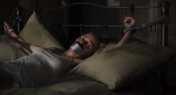 Movie still from “Goodnight Mommy” (2022), directed by Matt Sobel – A woman with a taped mouth laying in bed; Medium shot, High angle