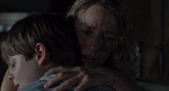 Movie still from “Goodnight Mommy” (2022), directed by Matt Sobel – A woman and a child are hugging in a dark room; Close Up shot, Over the shoulder angle