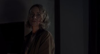 Movie still from “Goodnight Mommy” (2022), directed by Matt Sobel – A woman standing in a room with a dark background; Close Up shot, Over the shoulder angle