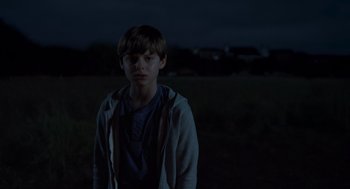 Movie still from “Goodnight Mommy” (2022), directed by Matt Sobel – A young boy standing in a field at night; Medium shot, Over the shoulder angle