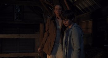 Movie still from “Goodnight Mommy” (2022), directed by Matt Sobel – A woman standing next to a young boy in a barn; Medium shot, Low angle