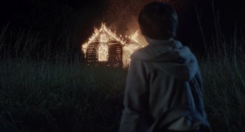 Movie still from “Goodnight Mommy” (2022), directed by Matt Sobel – A person standing in front of a burning house; Wide shot, Over the shoulder angle