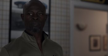 Movie still from “Gran Turismo” (2023), directed by Neill Blomkamp – A man with a beard is standing in a room; Close Up shot, Over the shoulder angle