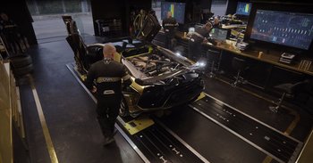 Movie still from “Gran Turismo” (2023), directed by Neill Blomkamp – A man standing in front of a car on a track; Wide shot, High angle