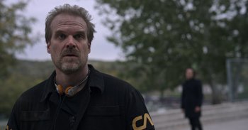 Movie still from “Gran Turismo” (2023), directed by Neill Blomkamp – A person wearing headphones near a tree; Close Up shot, Over the shoulder angle