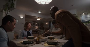 Movie still from “Gran Turismo” (2023), directed by Neill Blomkamp – Three people sitting at a dinner table with food; Medium shot, Over the shoulder angle