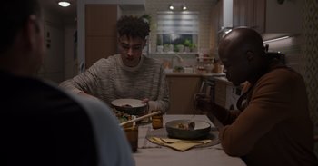 Movie still from “Gran Turismo” (2023), directed by Neill Blomkamp – A group of people sitting at a table eating food; Medium shot, Over the shoulder angle